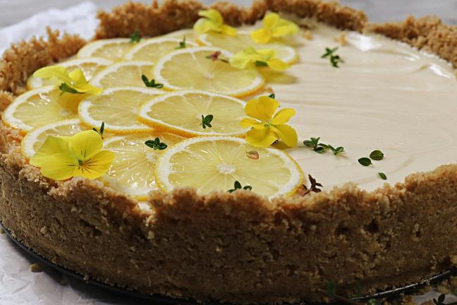 Side view of lemon cheesecake with sliced lemons and edible flowers.