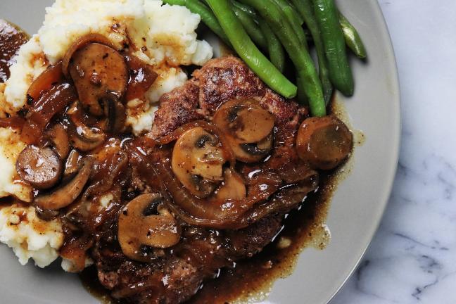 Salisbury steak with mushroom gravy served with mashed potatoes and green beans.