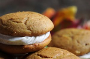 Soft pumpkin spice flavored cookies with creamy buttery vanilla filling on a plate with autumn leaves in the background.