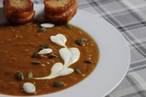 Creamy pumpkin soup in a bowl garnished with sour cream and pepitas served with little cheese sandwiches.