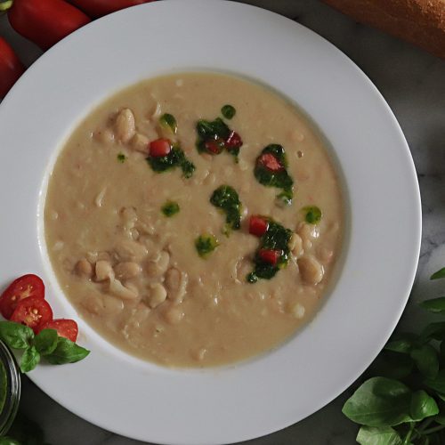 Creamy white bean soup with an herb sauce drizzled on top with basil and tomato as garnish.