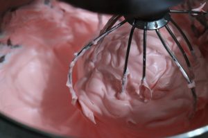 A stand mixer witha whisk attachment whipping lovely, pillowy pink meringue.