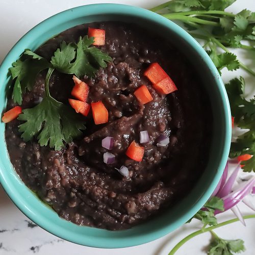 A bowl of creamy refried black beans with chopped tomato, green onion and cilantro on top.