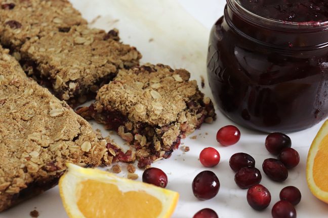 delicious cranberry oat bars with a crumble topping on a tray with a jar of homemade cranberry sauce with orange slices and fresh cranberries.