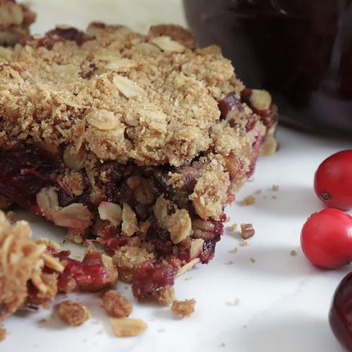 delicious cranberry oat bars with a crumble topping on a tray with a jar of homemade cranberry sauce with orange slices and fresh cranberries.