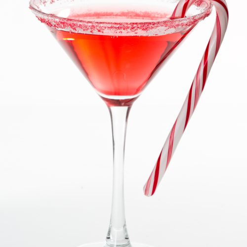 A stylish martini glass with a pink martini that's made with candy cane vodka. There's a little peppermint candy cane hanging on the side of the glass and it's cute!