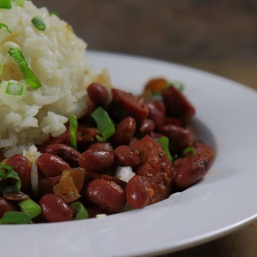 A plate filled with delicious red beans and rice. There are pieces of sausage and celery along with onion, and bell peppers. juicy and delicious!