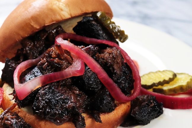 Delicious Poor Man’s Burnt Ends piled high on a warm toasted bun, topped with tangy pickled onions and crisp bread-and-butter pickles, served on a plate for the perfect BBQ bite.