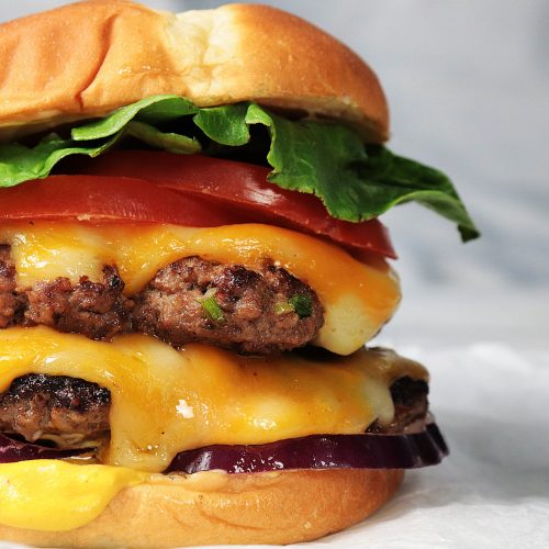 A perfectly cooked, juicy hamburger stacked with melted cheese, fresh lettuce, tomato, and pickles, all nestled in a lightly toasted bun, ready to be devoured.