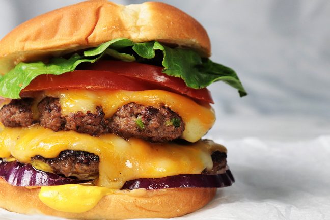 A perfectly cooked, juicy hamburger stacked with melted cheese, fresh lettuce, tomato, and pickles, all nestled in a lightly toasted bun, ready to be devoured.