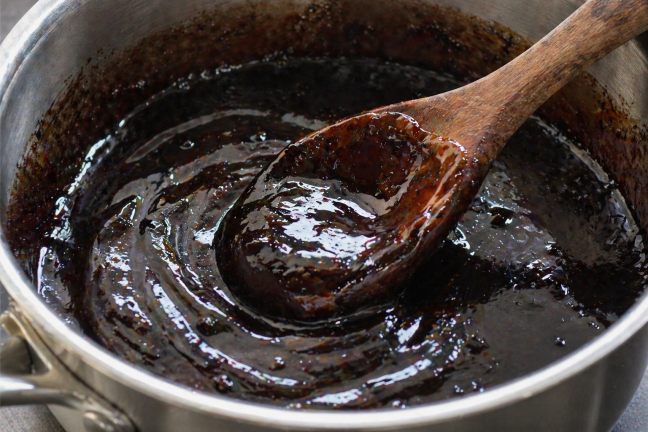 A close-up of dark, rich balsamic and brown sugar glaze being stirred in a small saucepan, showing a thick, syrupy consistency with a glossy sheen.