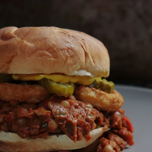 A delicious sloppy joe sandwich, served on a hamburger bun, made with lentils simmered with veggies in a sweet and tangy BBQ style sauce. Served with onion rings and bread and butter pickles. Divine!