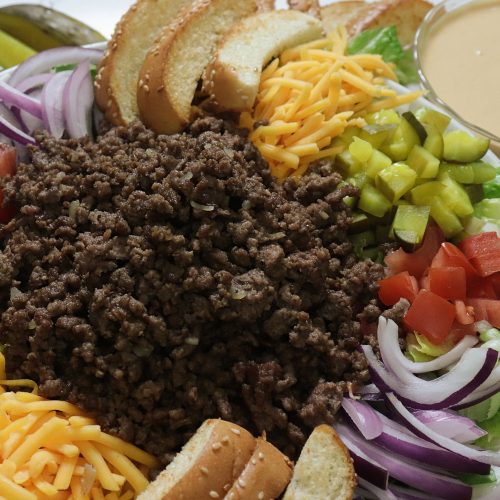 A bowl full of delicious hamburger inspired salad with ground beef. onion, tomato and lots of dill pickles with a "secret sauce" you'll remember from your favorite hamburger.