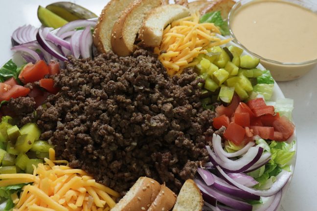 A bowl full of delicious hamburger inspired salad with ground beef. onion, tomato and lots of dill pickles with a "secret sauce" you'll remember from your favorite hamburger.