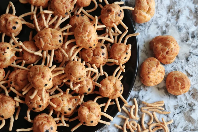 A plate filled with round pate a choux pastries with chow mein noodles pressed in to look like cute little spiders for Halloween. Cute!